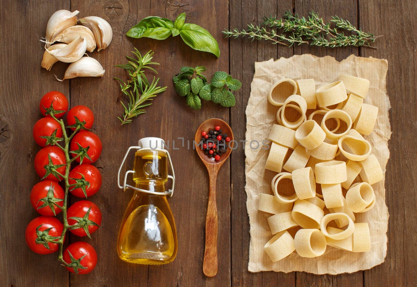 Italian pasta, vegetables, herbs and olive oil on wooden background