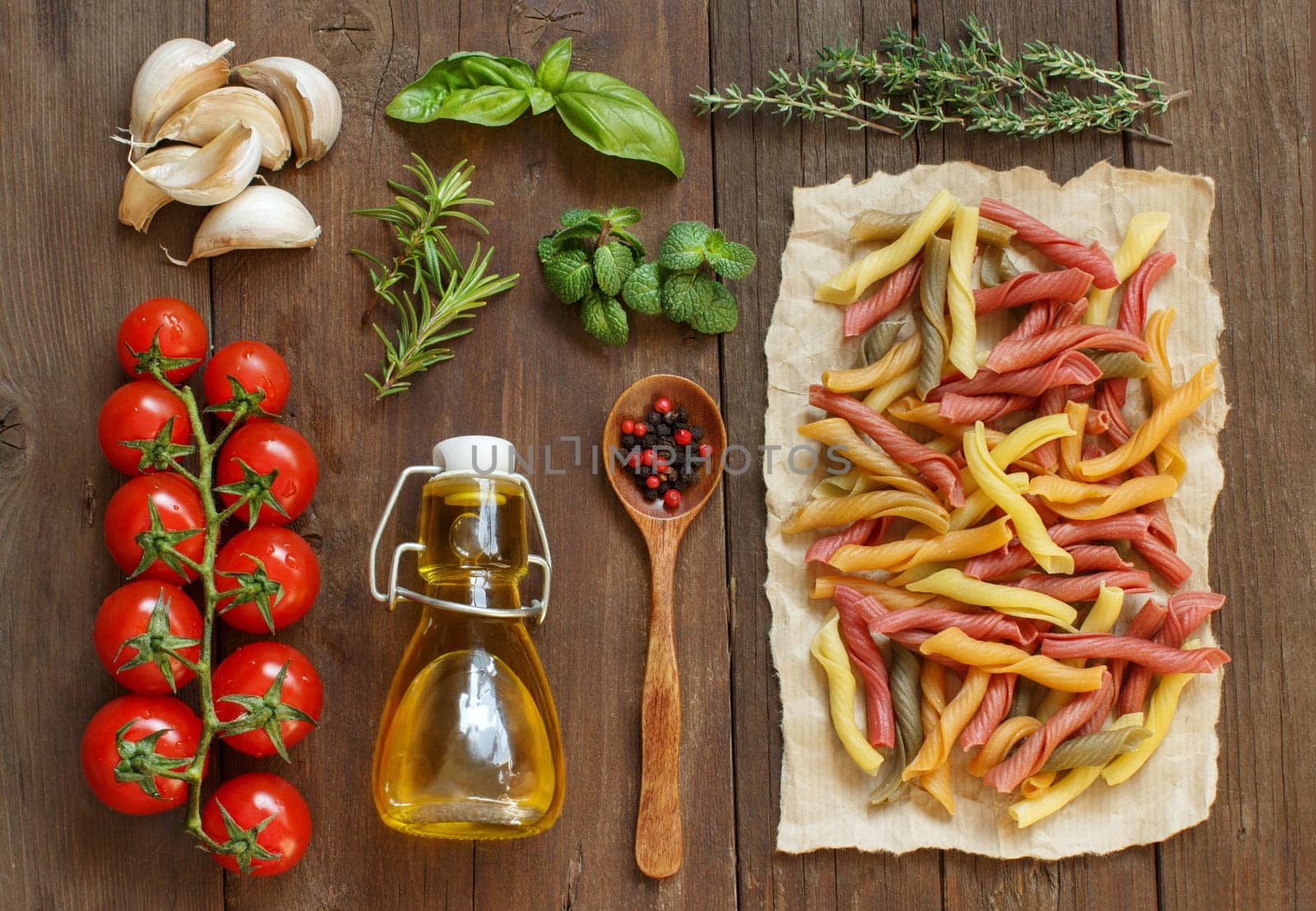 Whole wheat pasta, vegetables, herbs and olive oil on wooden background