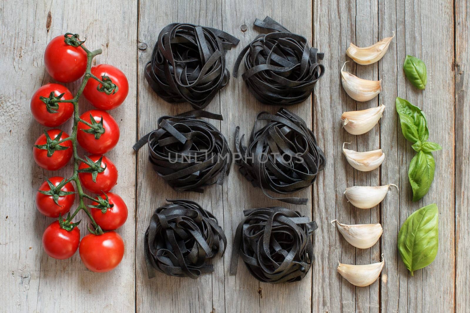 Dry Black Tagliatelle pasta with cherry tomatoes, garlic and basil on wood