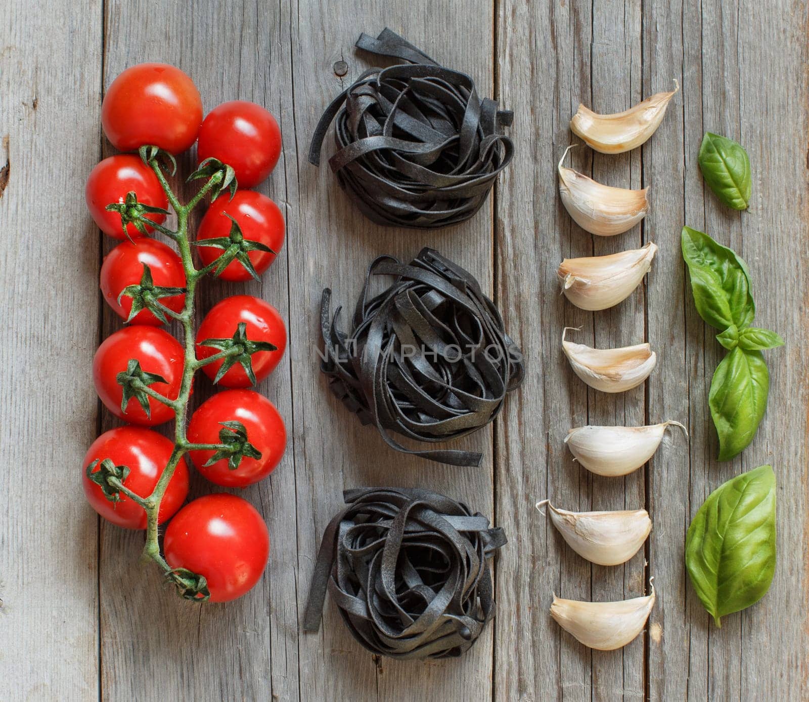 Dry Black Tagliatelle pasta with cherry tomatoes, garlic and basil on wood