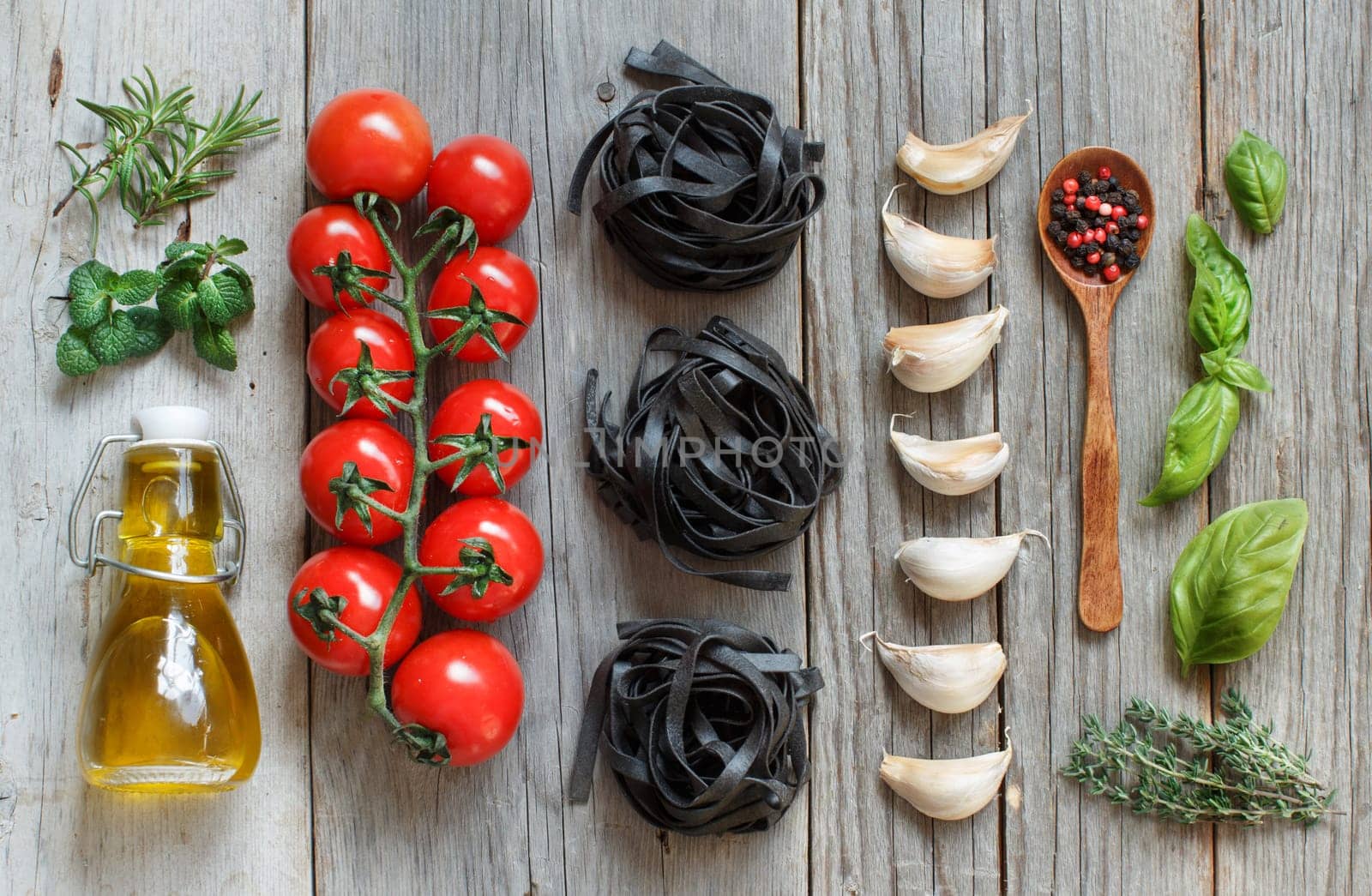Dry Black Tagliatelle pasta with cherry tomatoes, garlic and herbs on wood