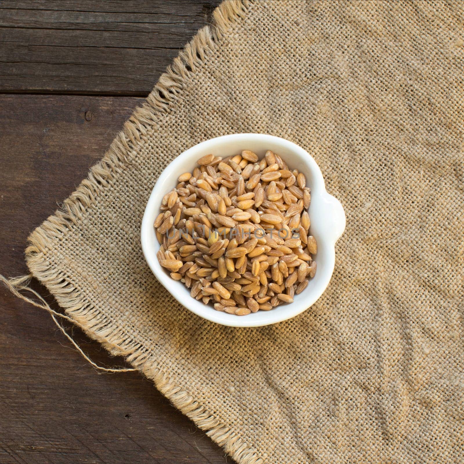 Whole unpolished spelt in a bowl on wood