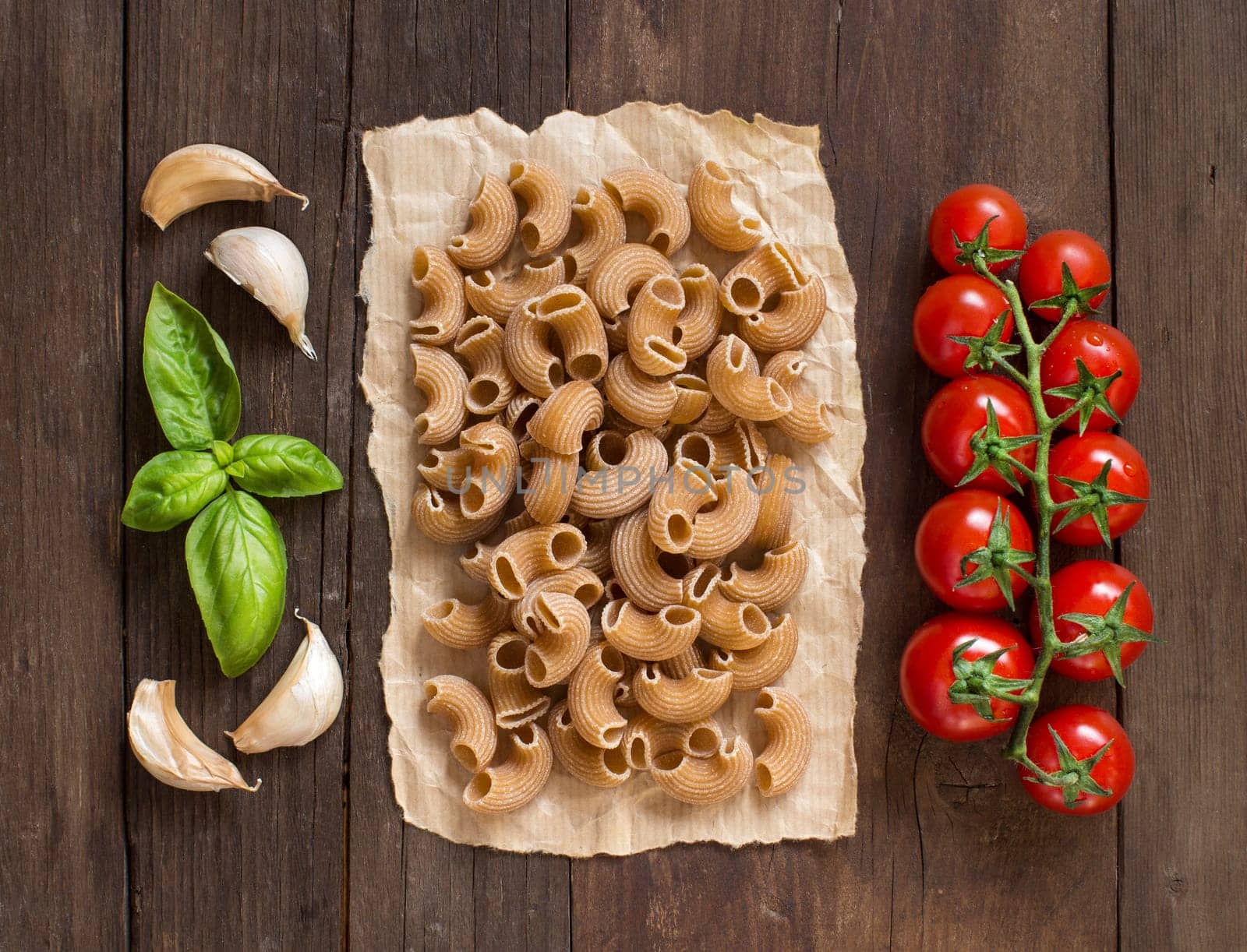Whole wheat pasta with garlic, tomatoes and basil on wooden background