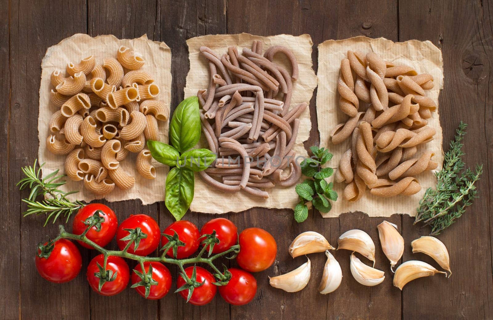Whole wheat pasta, vegetables, herbs and olive oil on wooden background