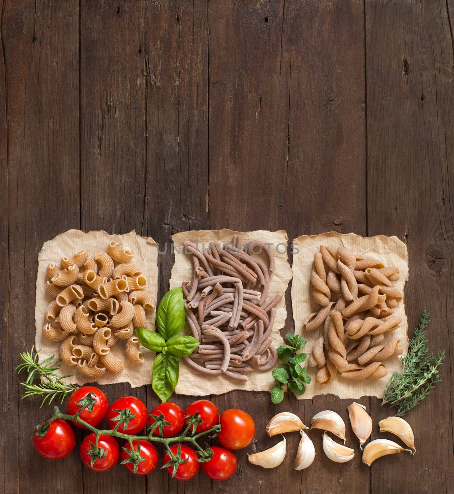 Whole wheat pasta with herbs and vegetables on a wooden background
