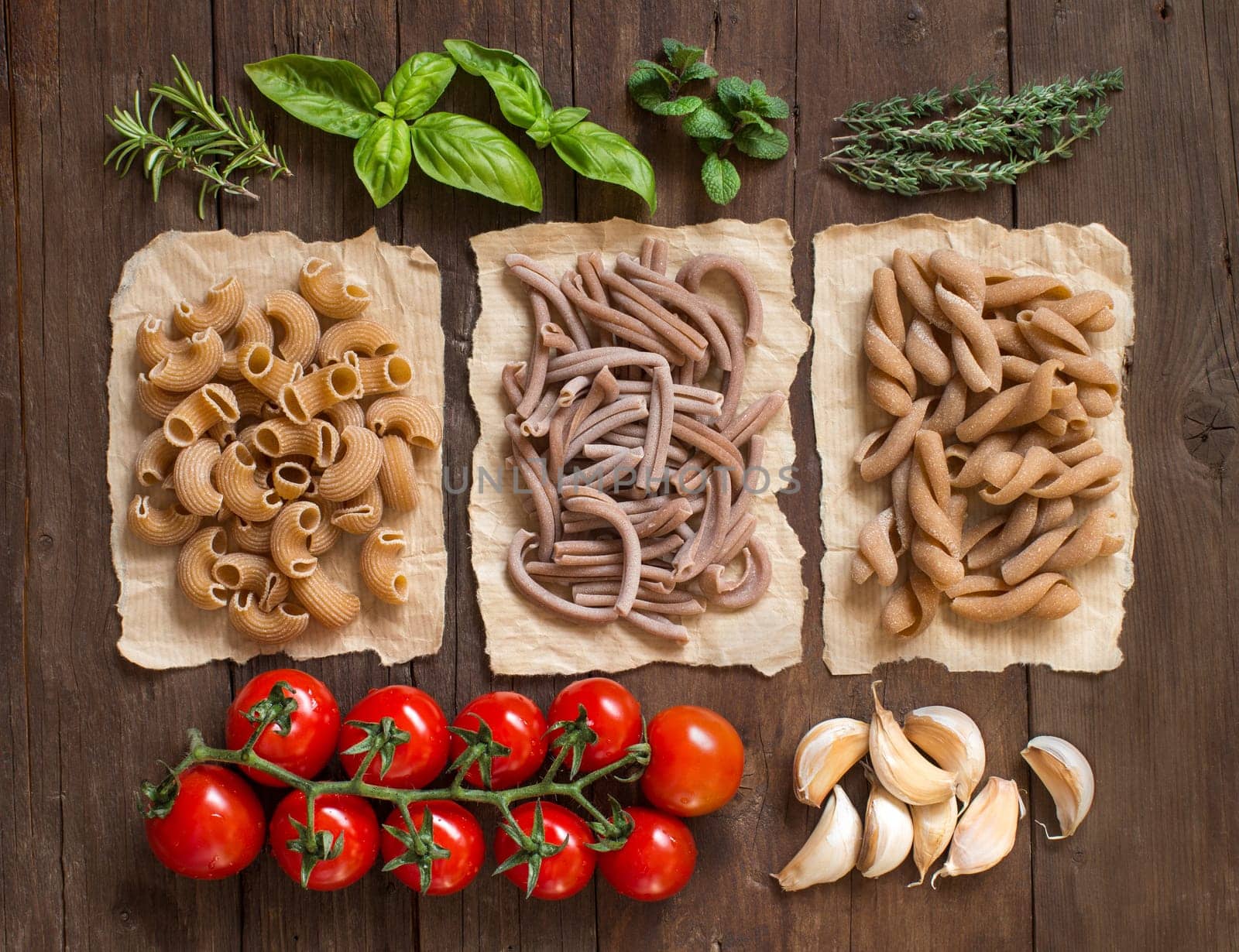 Whole wheat pasta, vegetables, herbs and olive oil on wooden background