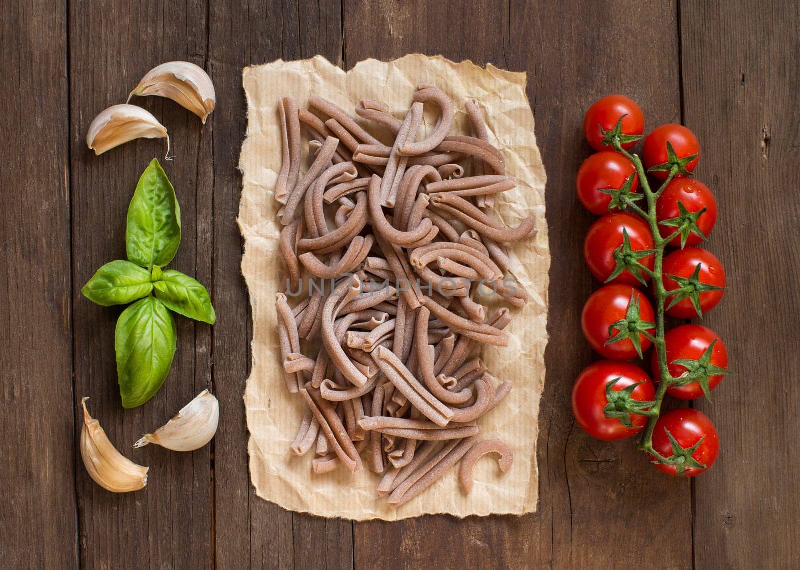 Whole spelt pasta, tomatoes, garlic and basil on wooden background