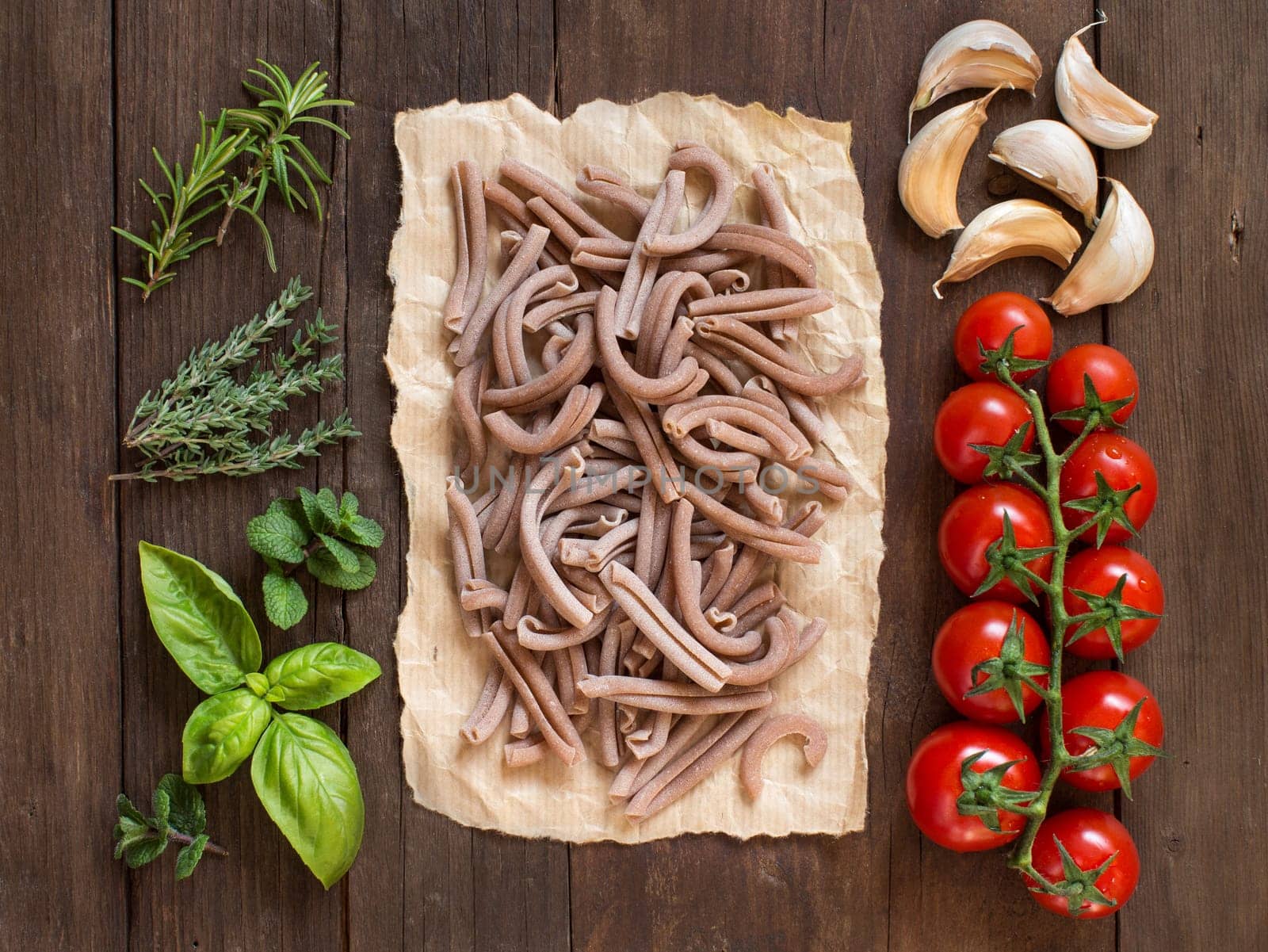 Whole spelt pasta, vegetables, herbs and olive oil on wooden background