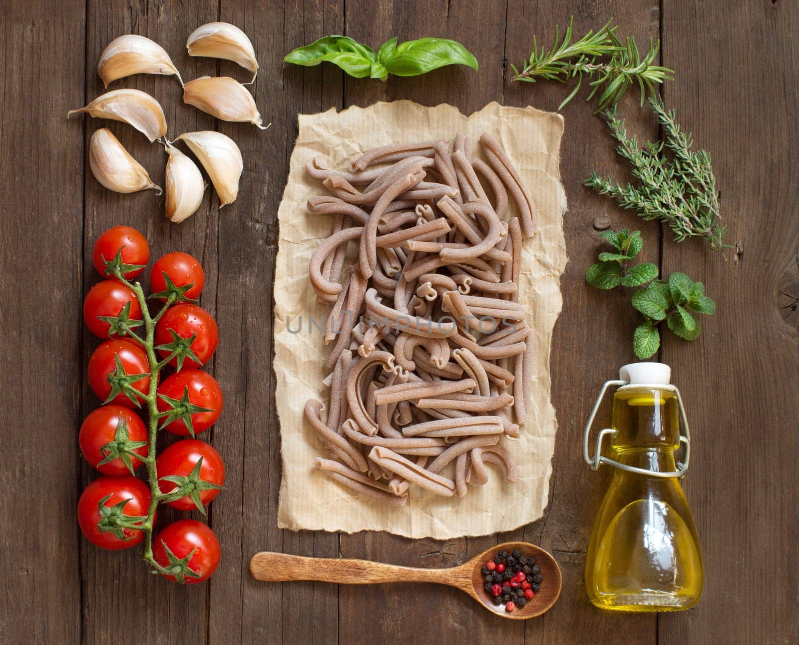 Whole spelt pasta, vegetables, herbs and olive oil on wooden background