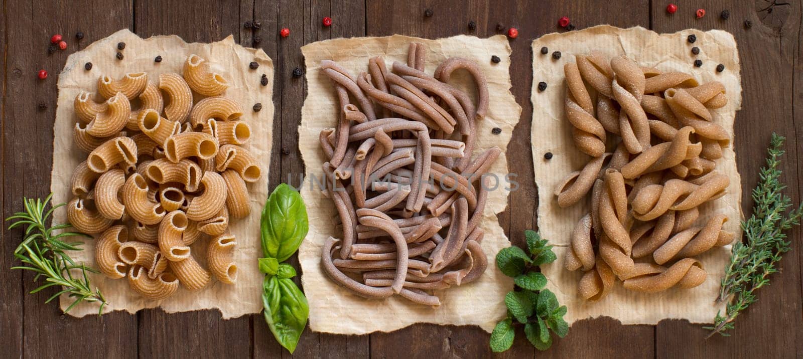 Whole wheat pasta and herbs on a wooden background