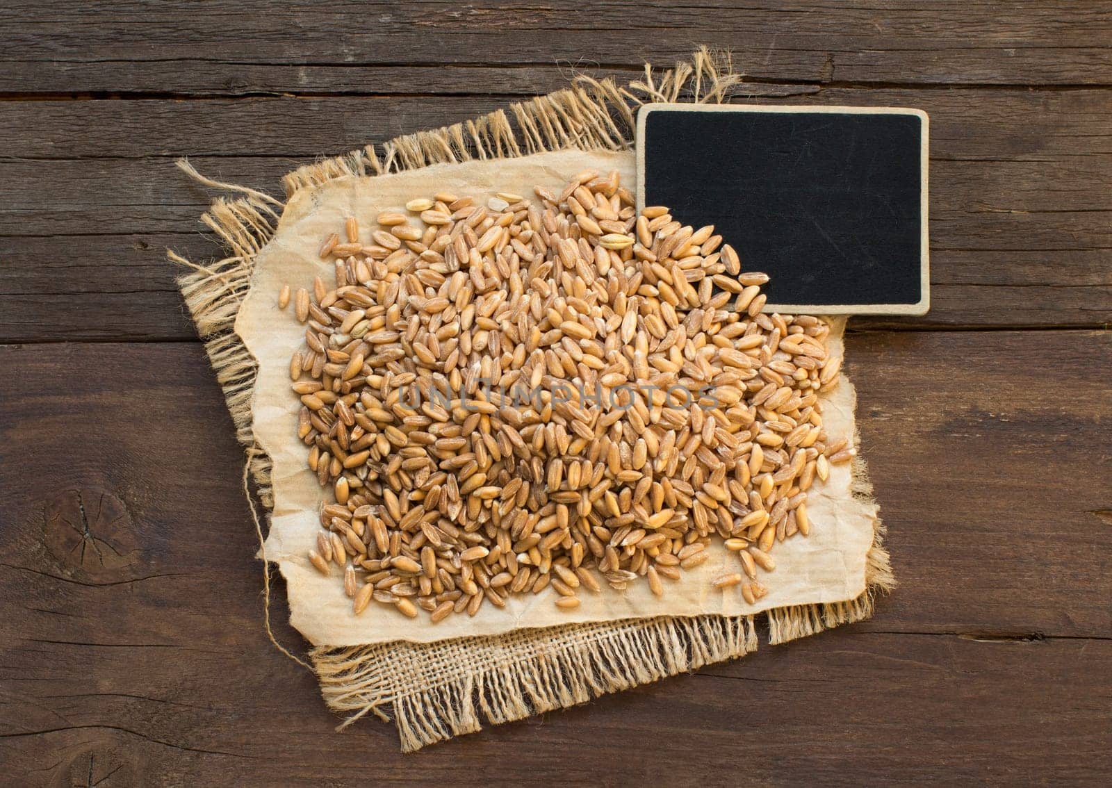 Whole unpolished spelt in a with a small chalkboard on wooden table