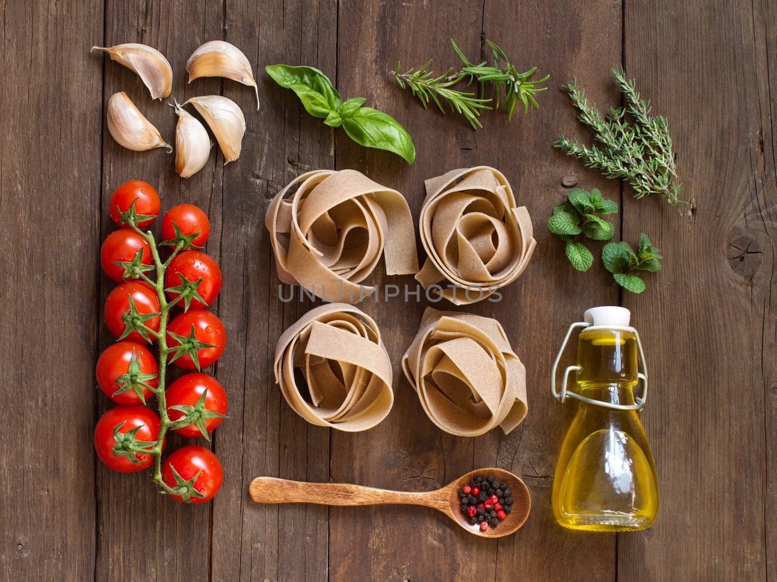 Whole wheat pasta, vegetables, herbs and olive oil on wooden background
