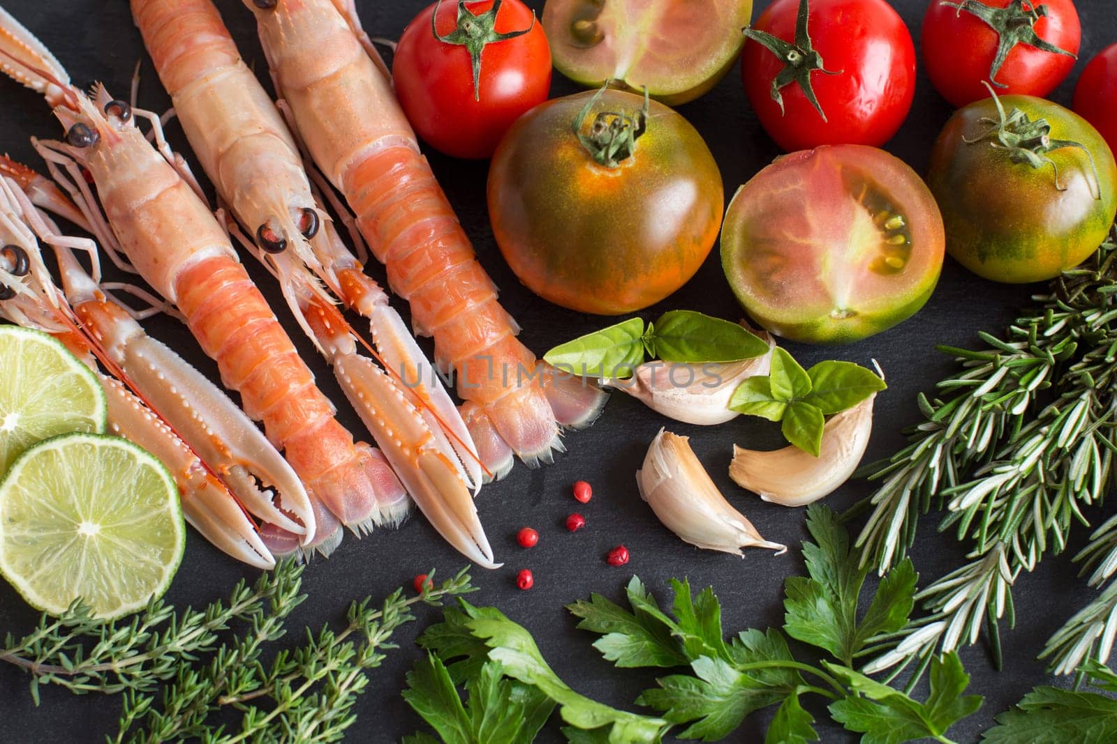 Raw langoustines with vegetables and herbs on the dark background