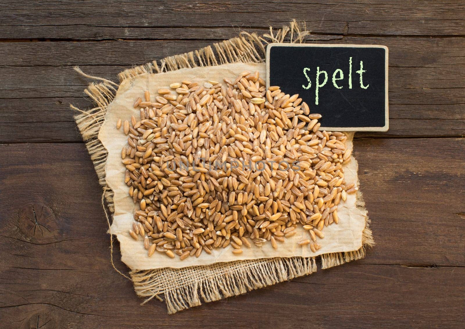 Whole unpolished spelt in a with a small chalkboard on wooden table