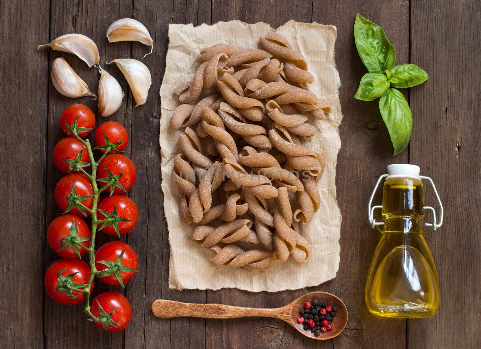 Whole wheat pasta, vegetables, herbs and olive oil on wooden background
