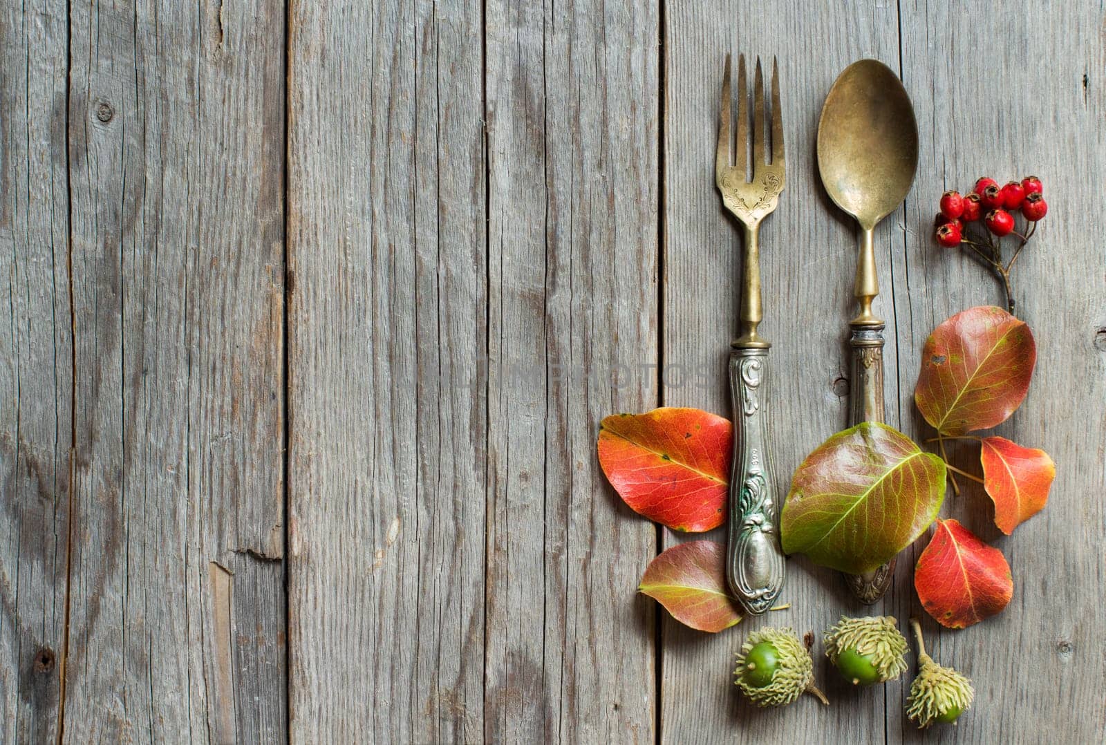 Vintage fork and knife with fall leaves, acorns and berries on the old wooden table