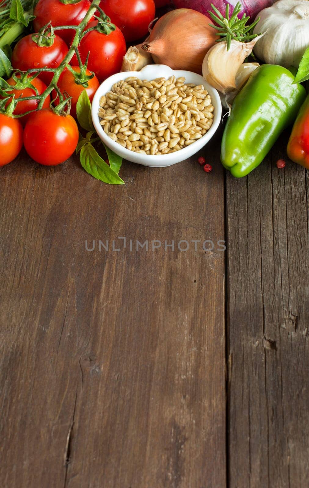 Spelt in a bowl and fresh vegetables on a wooden table