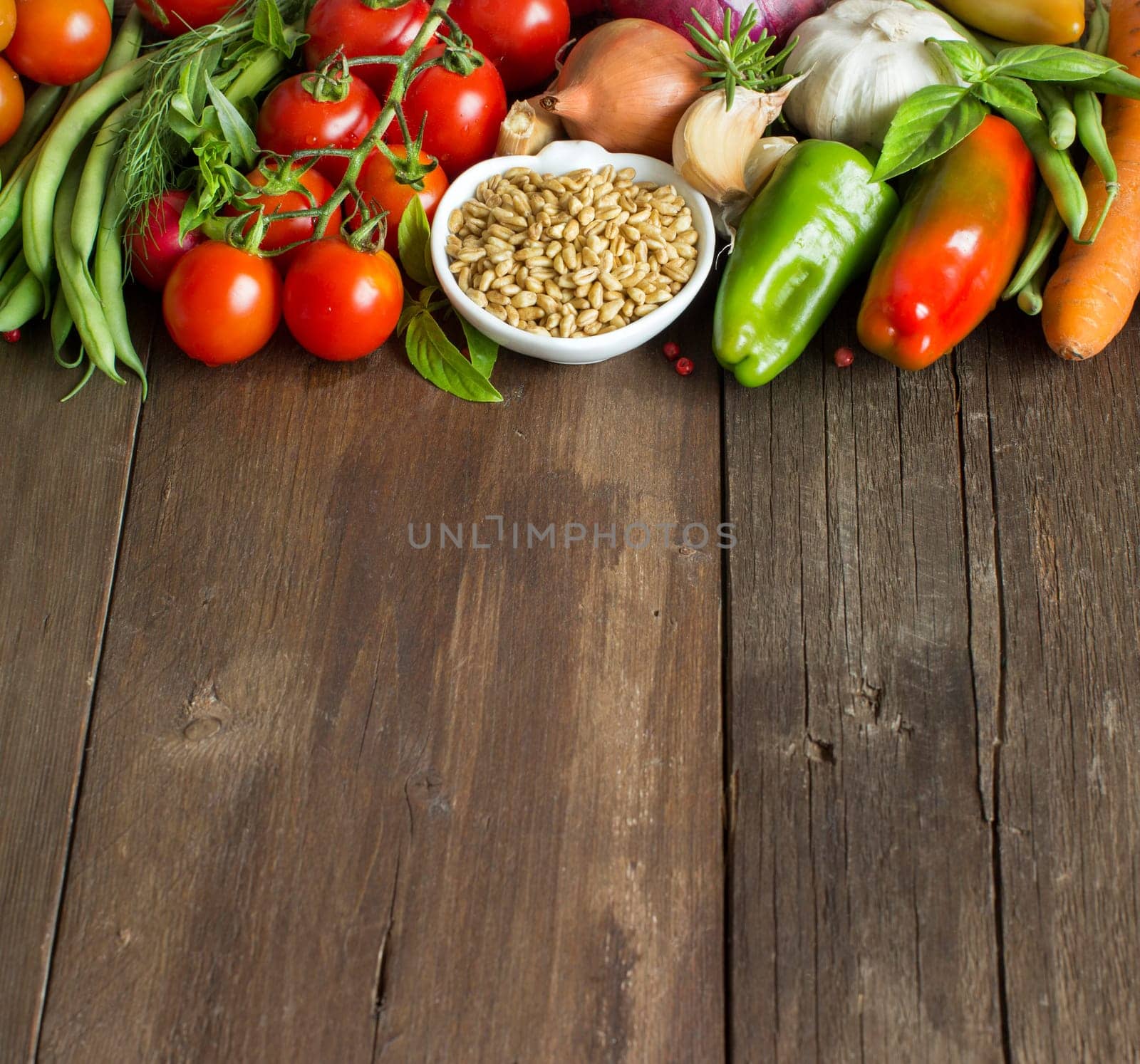 Spelt in a bowl and fresh vegetables on a wooden table