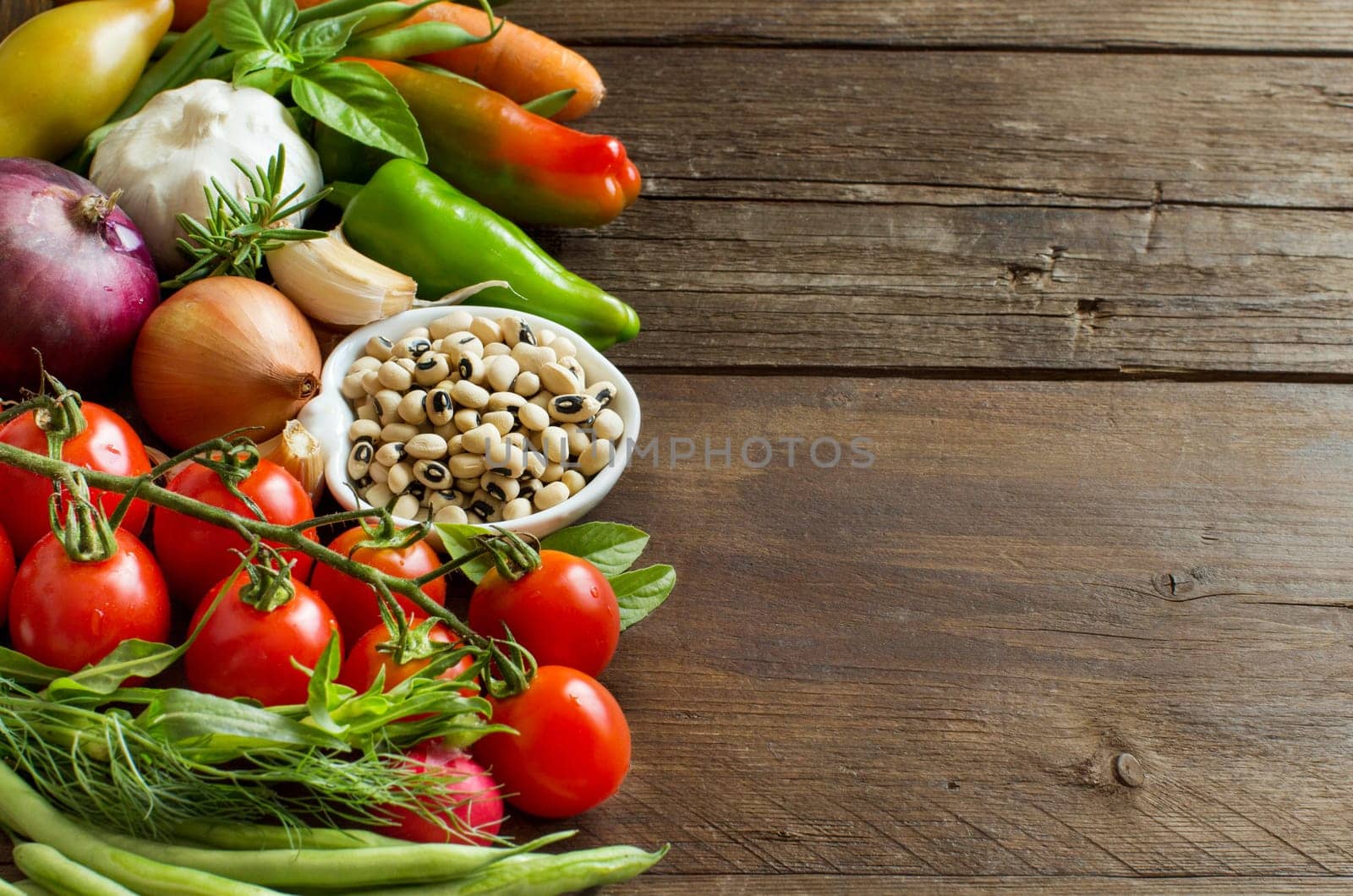 Black eyed peas in a bowl and vegetables on wood