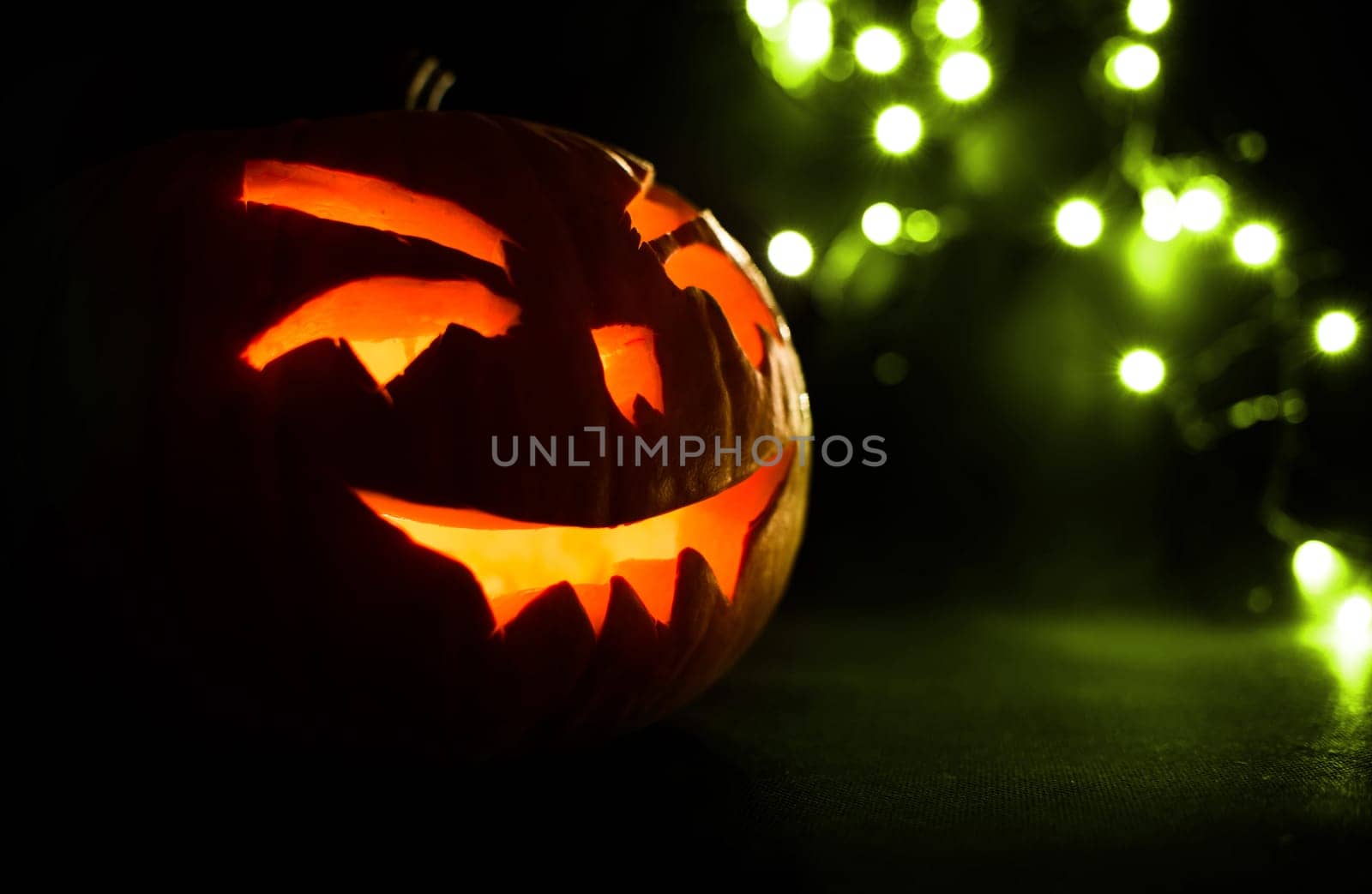 carved face of pumpkin glowing on halloween on green bokeh light background