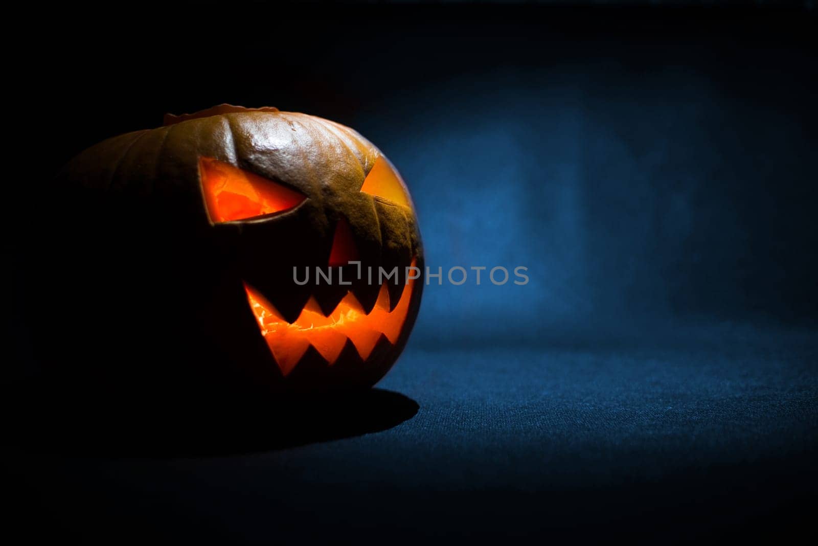 the carved face of pumpkin glowing on halloween on blue background