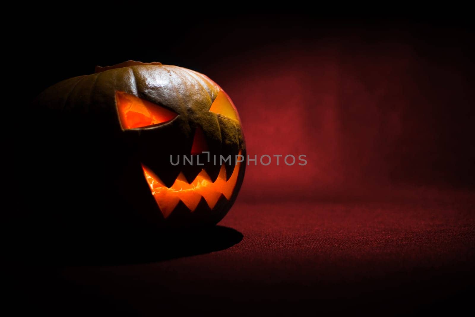 the carved face of pumpkin glowing on halloween on red background