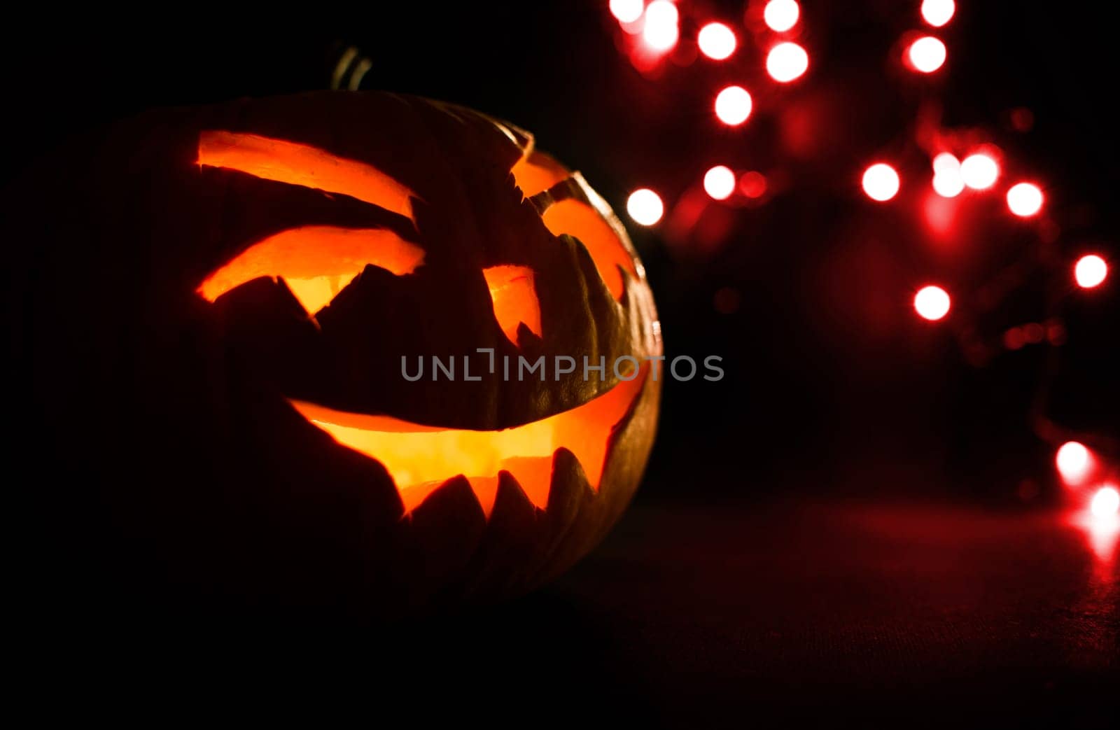 carved face of pumpkin glowing on halloween on red light background bokeh