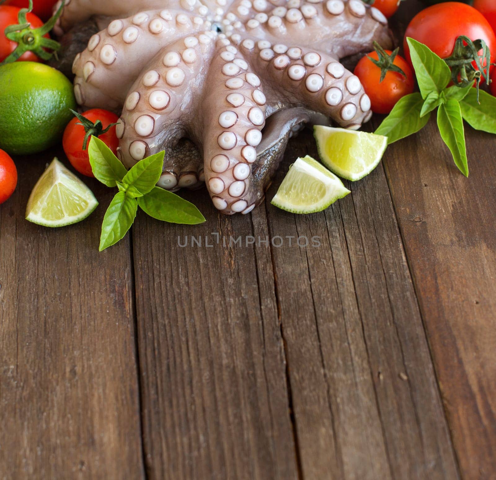 Raw octopus with lime, tomatoes and herbs over wooden background