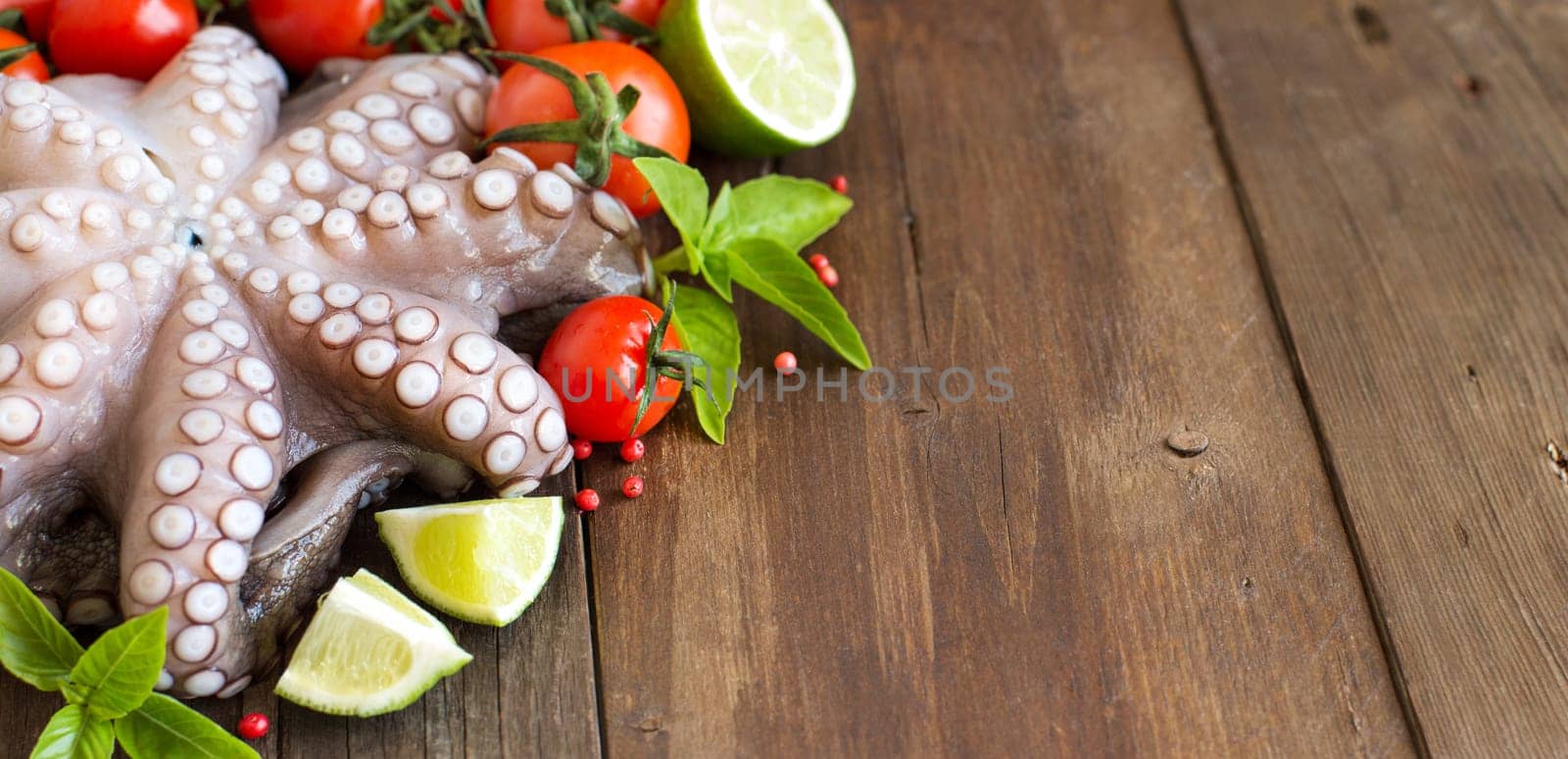 Raw octopus with lime, tomatoes and basil over wooden background