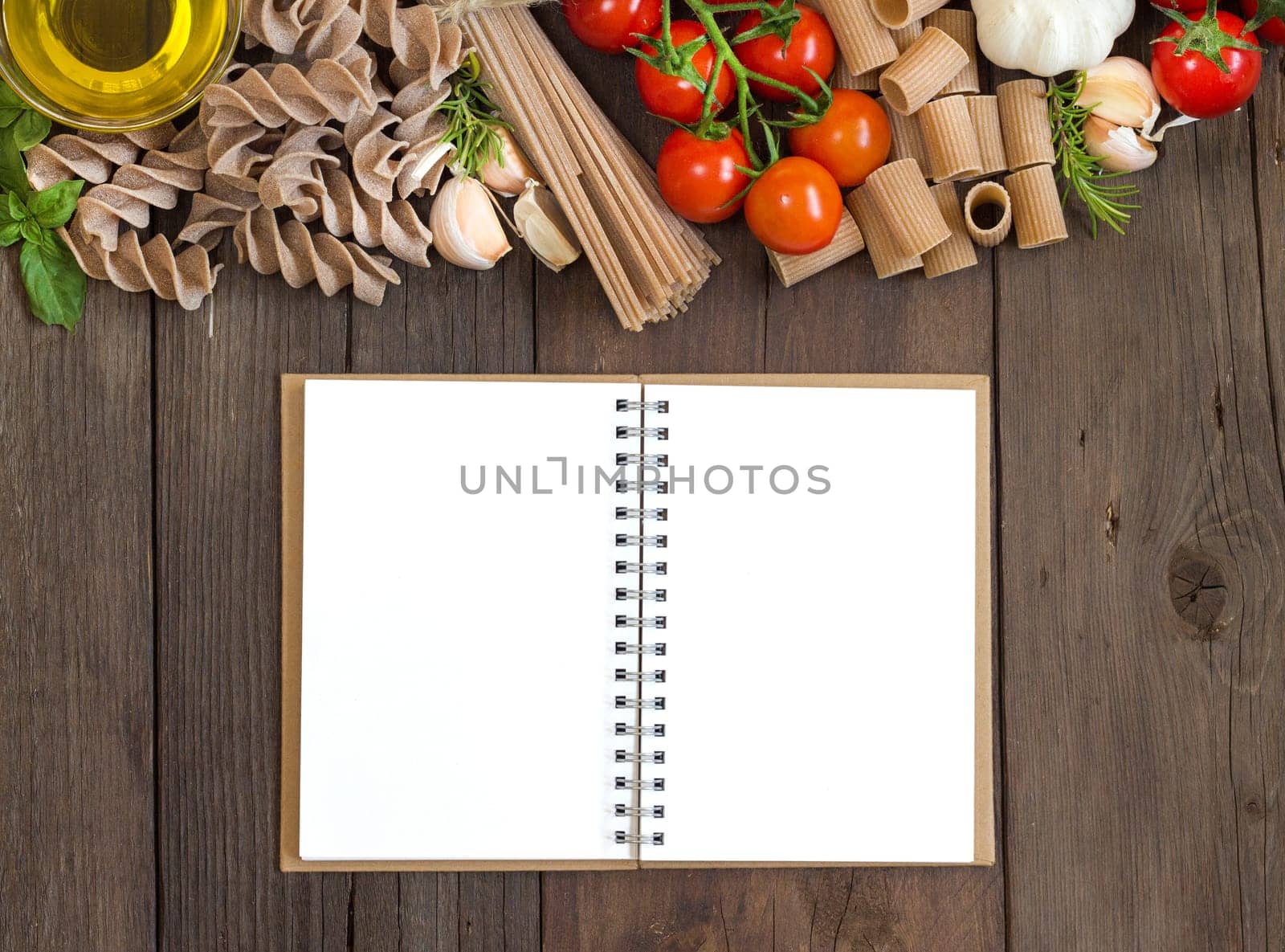 Olive oil, pasta, garlic and tomatoes with blocknote on the wooden table