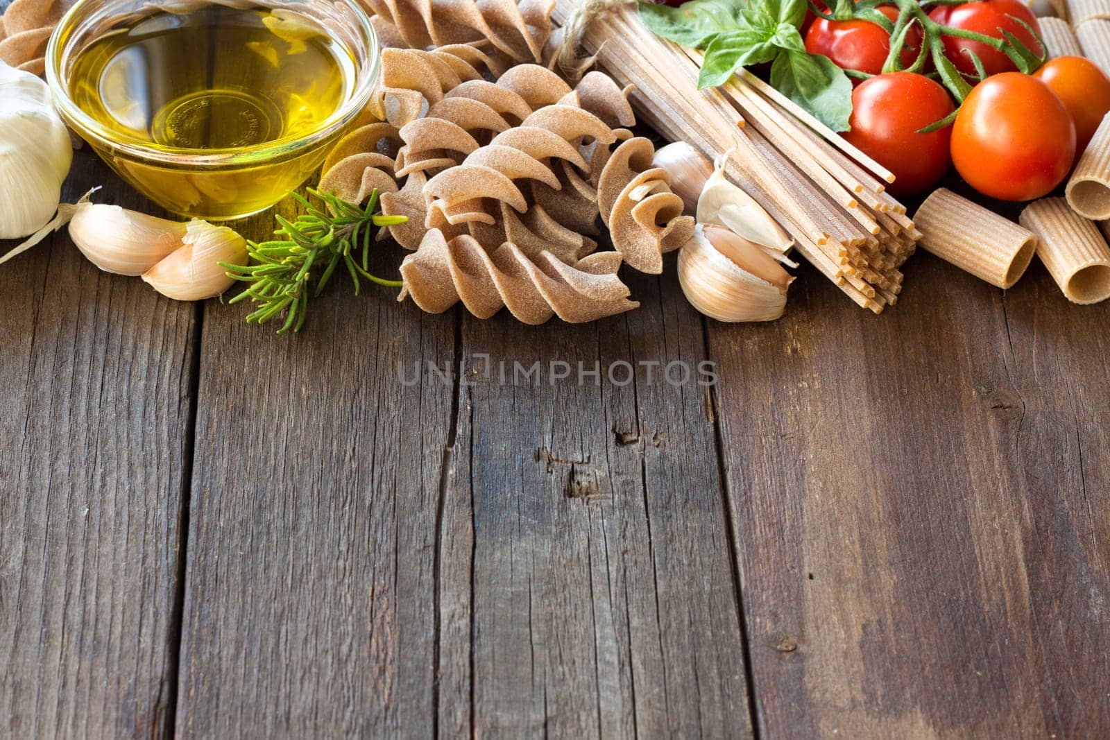 Olive oil, pasta, garlic and tomatoes on the wooden table