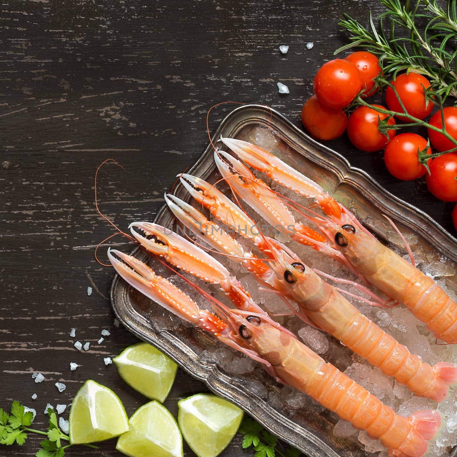 Raw langoustines on ice with lime,tomatoes and herbs over dark background