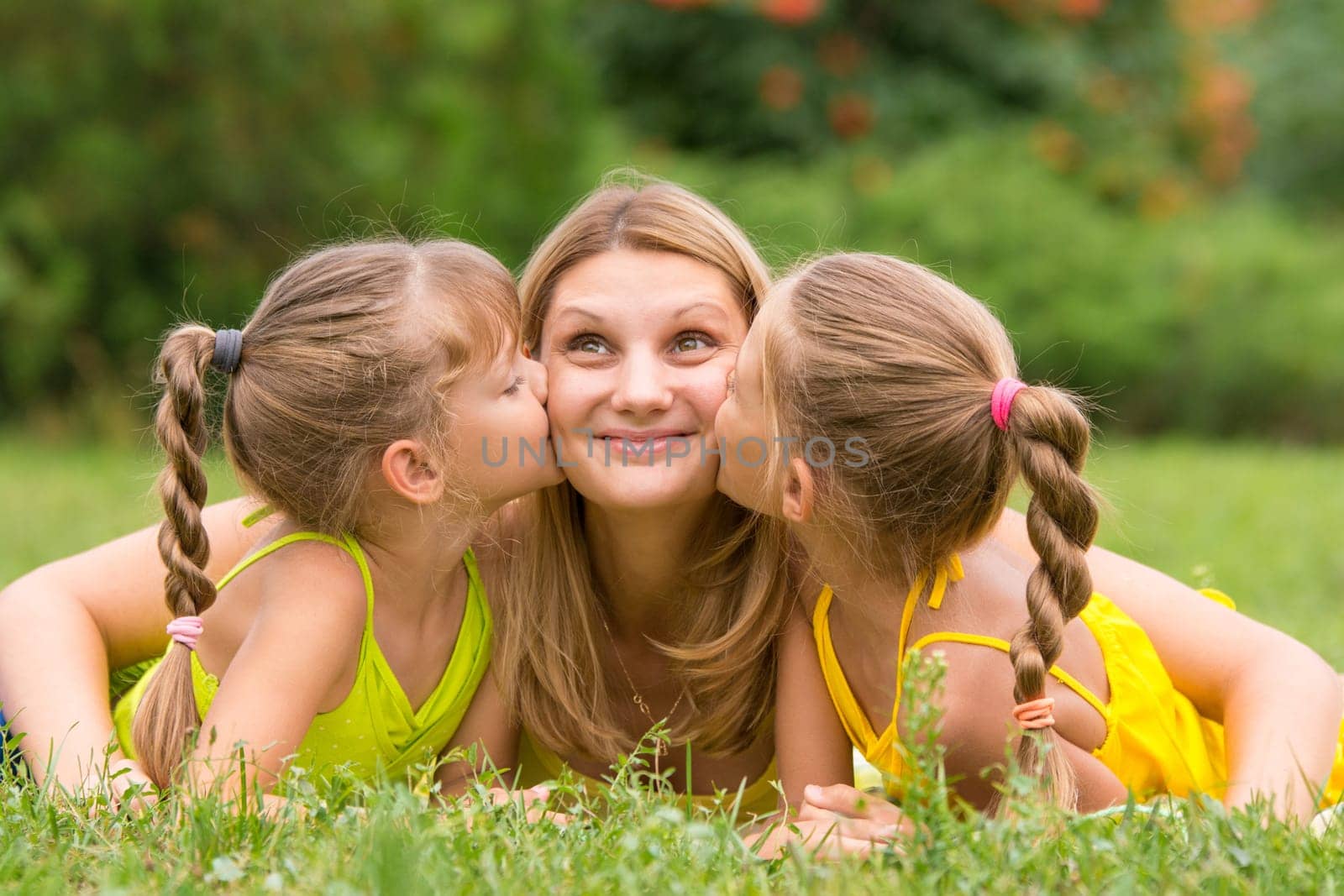 Two daughters kissing mother lying on the grass on a picnic, Mother looked up fun