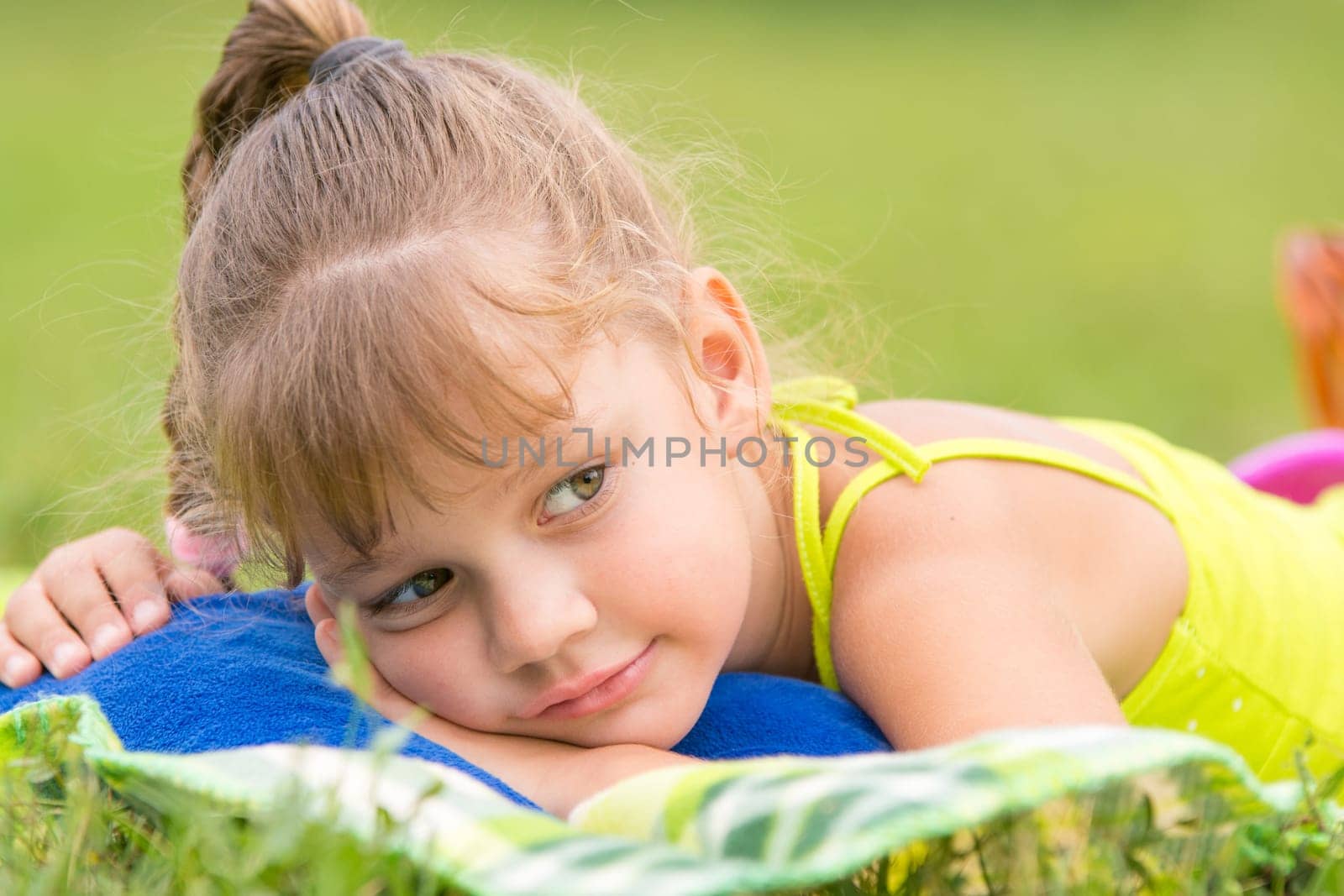 Five-year girl lies on a bed on a green meadow and thoughtfully looks aside