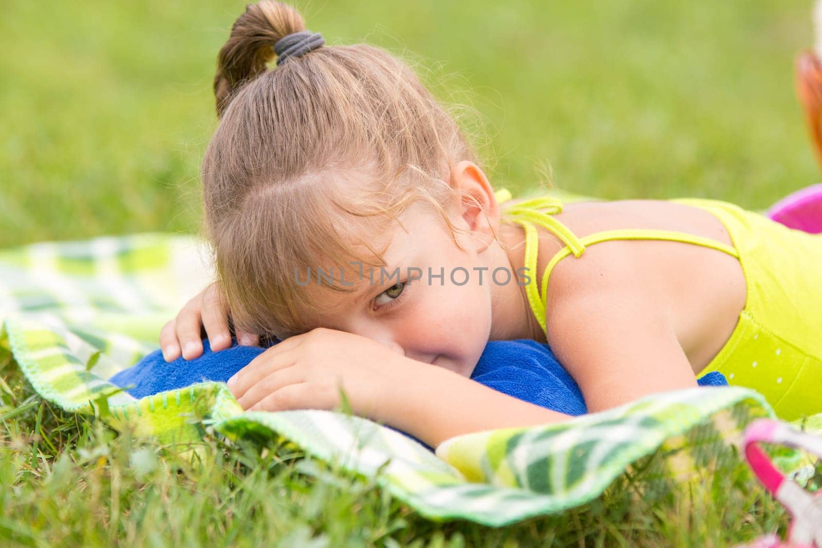 Five-year girl lies on a bed on a green meadow and artfully looks aside