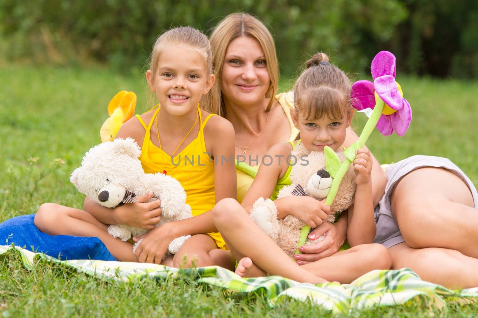 Young mother sitting on a picnic in a clearing with two daughters