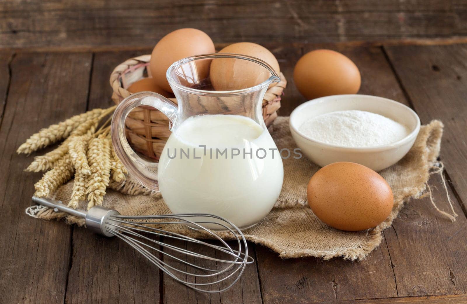 Milk, flour, wheat, whisk and eggs on the old wooden table