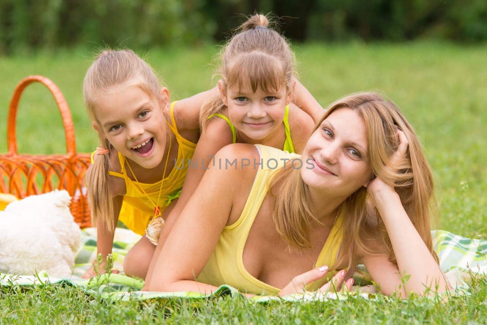 Mother and two daughters lie on each other on the green grass