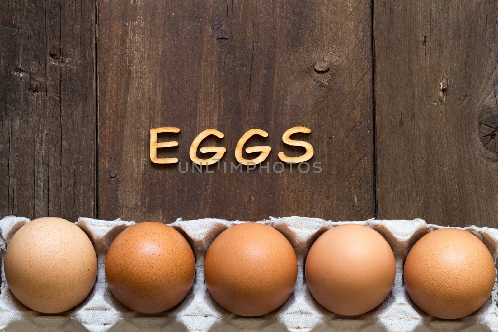 Chicken eggs in the package and the word EGGS on wood