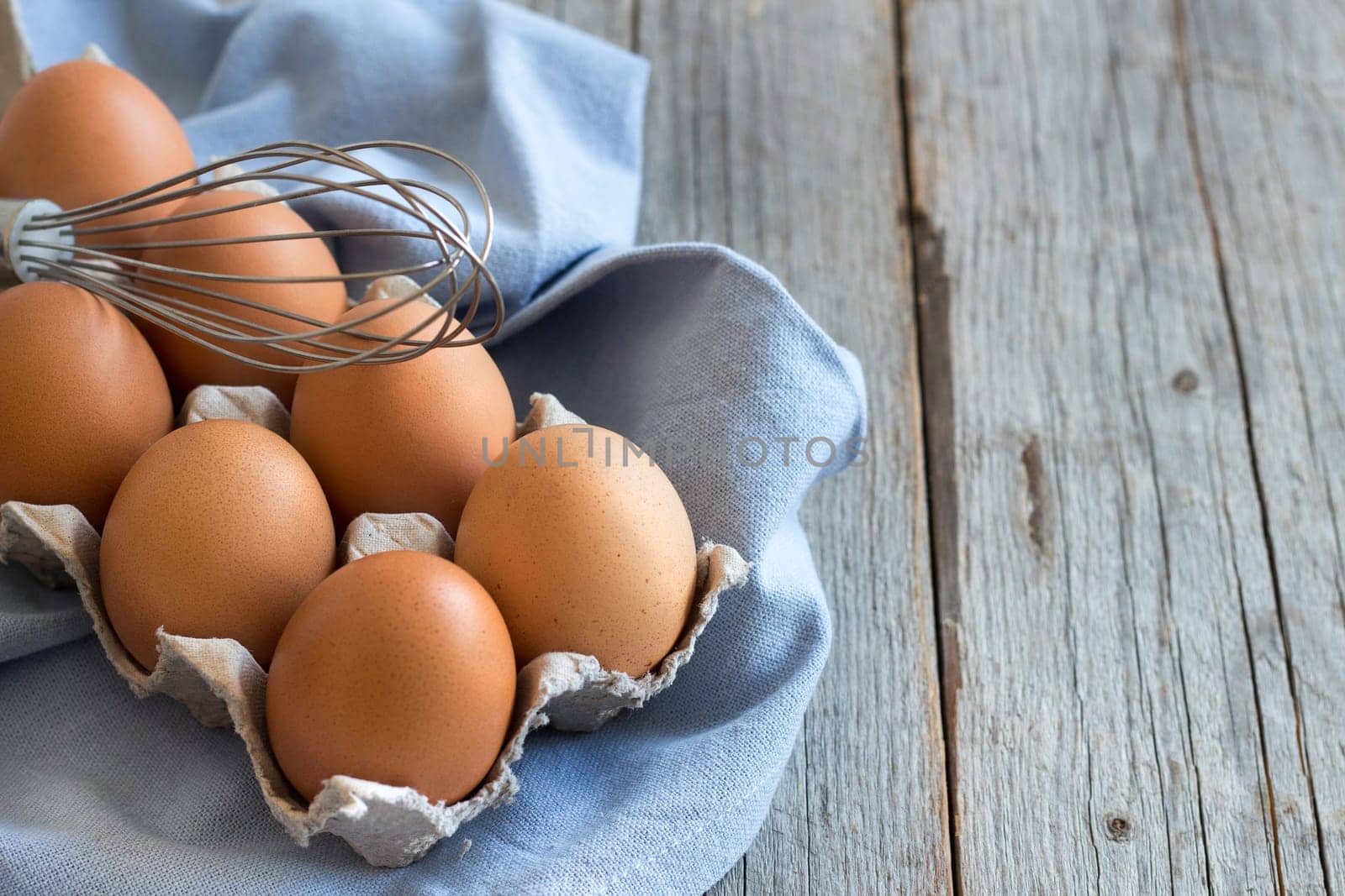 Chicken eggs in the box and whisk on the blue napkin