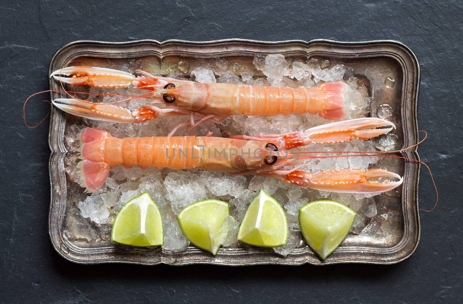 Raw langoustine with lime on ice on a silver tray