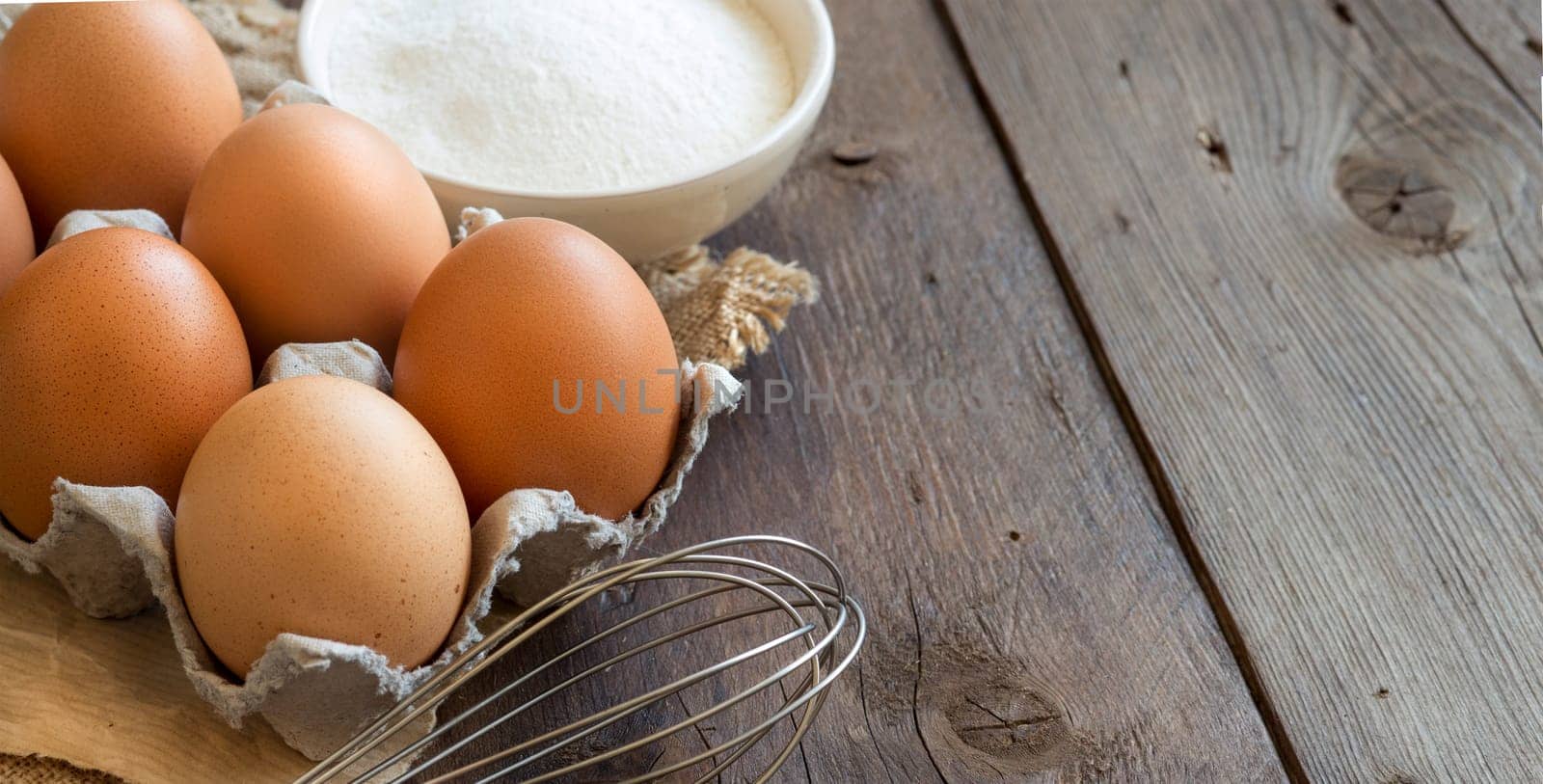 Chicken eggs, flour and whisk on the old wooden table