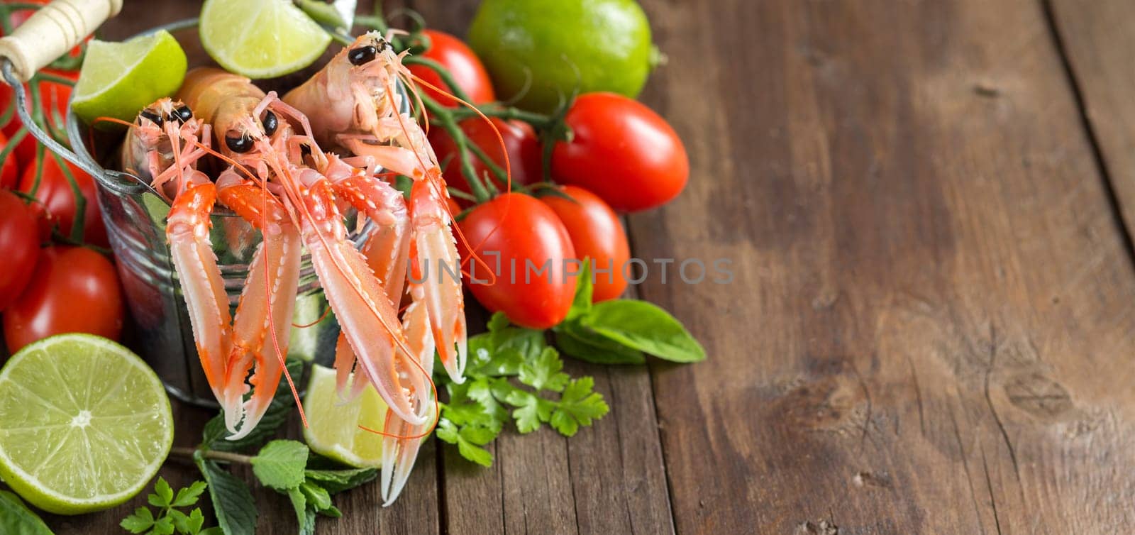 Raw langoustine in a bucket with vegetables and herbs on wood