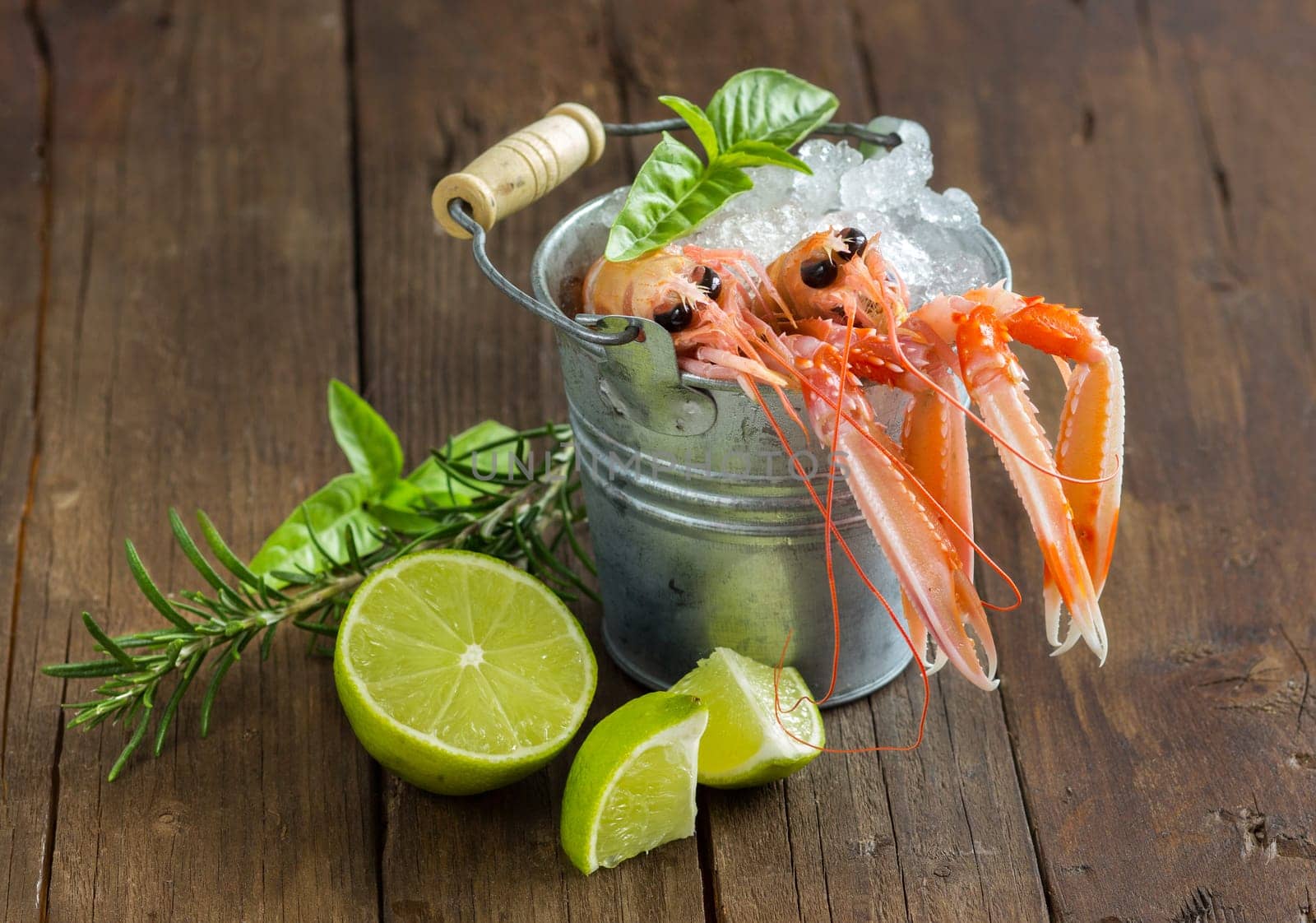 Raw langoustine in a bucket with vegetables and herbs on wood