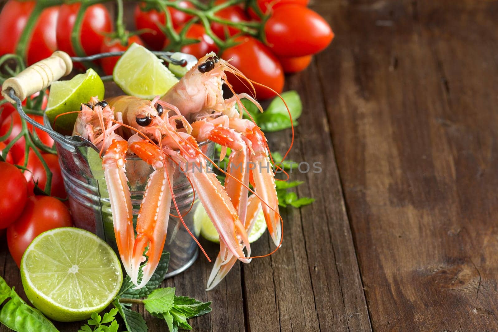 Raw langoustine in a bucket with vegetables and herbs on wood