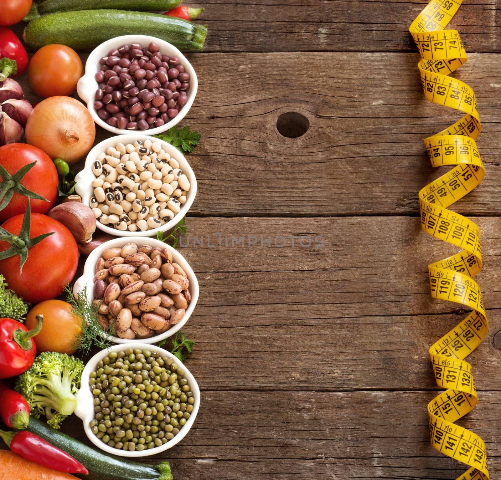 Legumes in bowls and vegetables on a wooden table