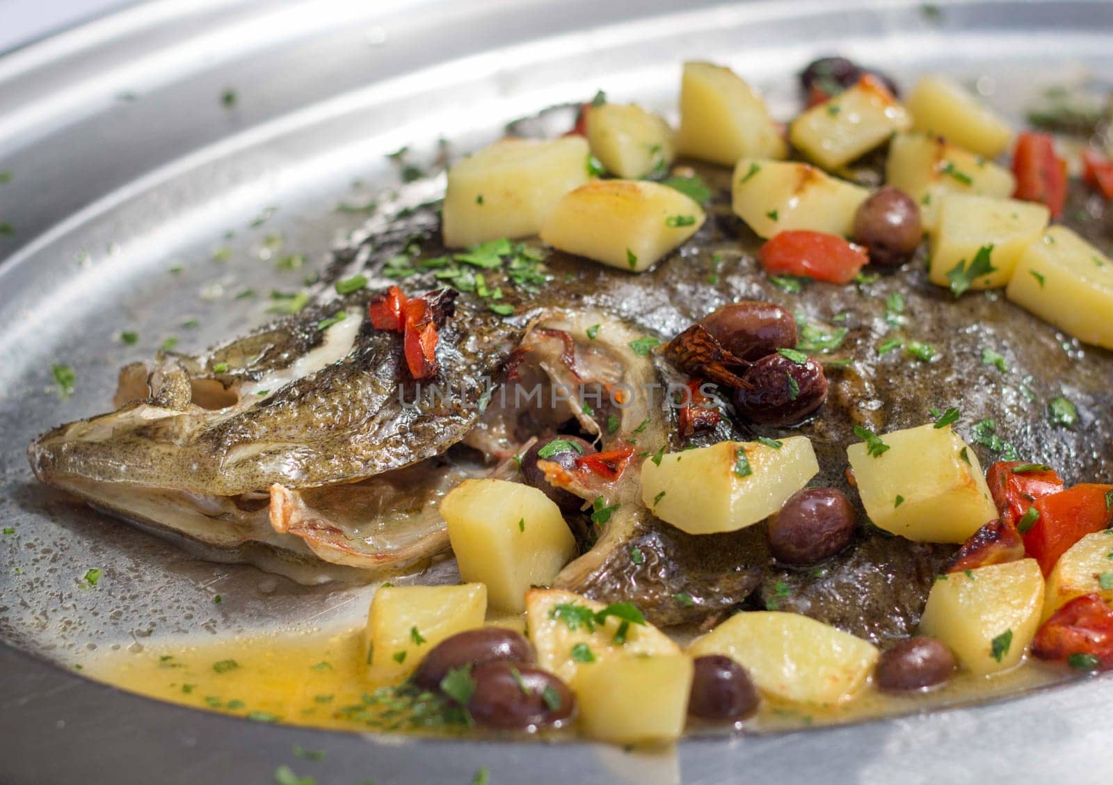 Baked flounder fish with potatoes, olives and tomates cooked in oven