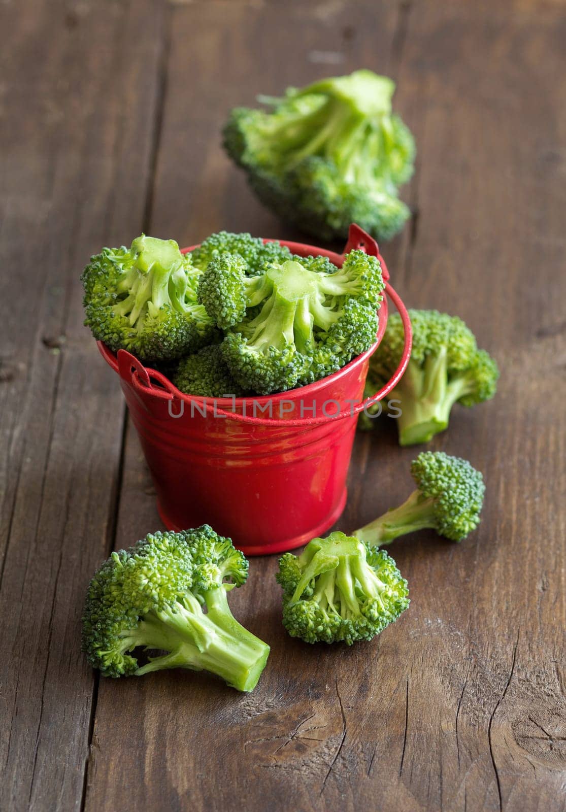 Green broccoli in red bucket on old wood