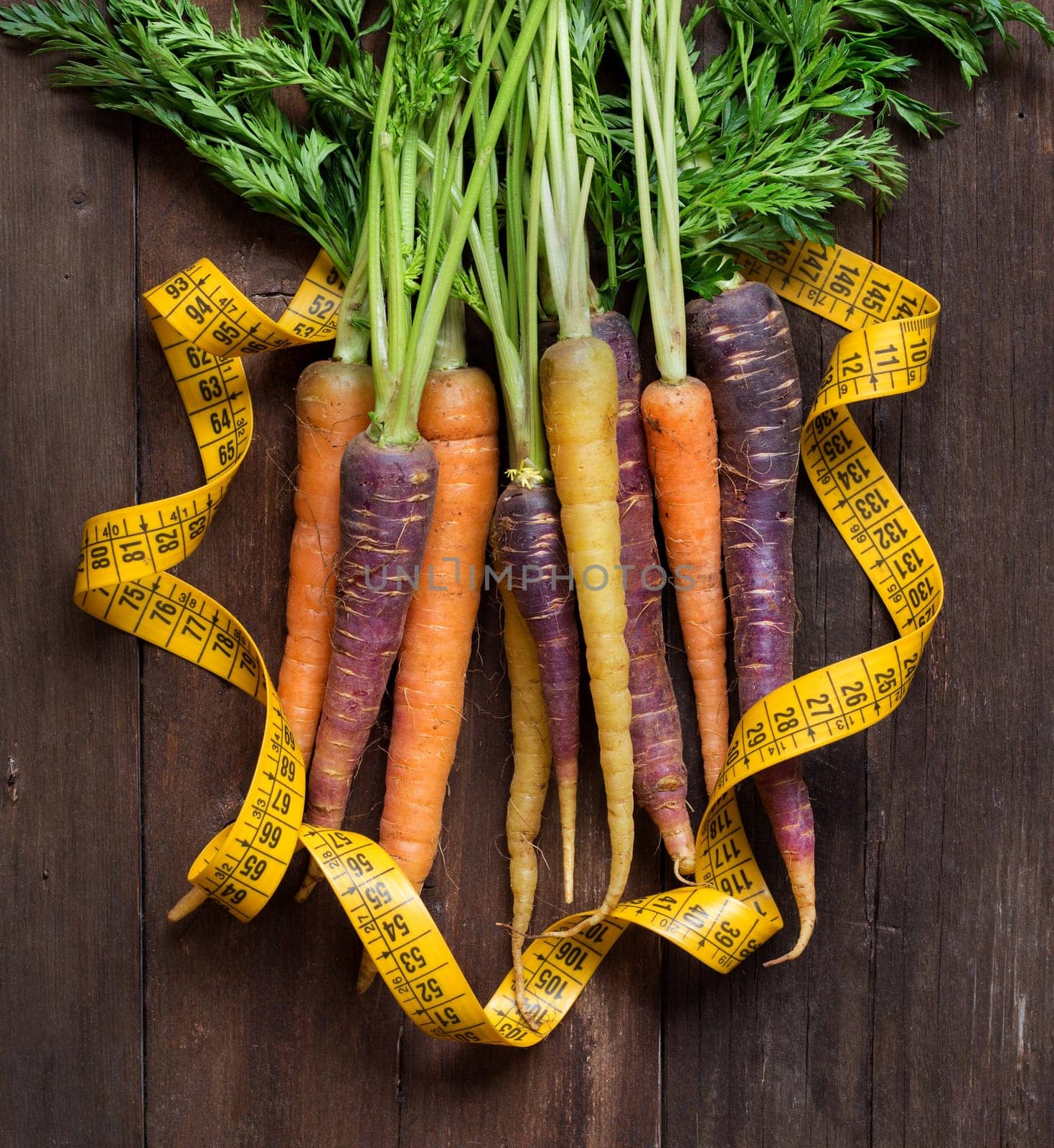 Fresh organic rainbow carrots and yellow measuring type on wood