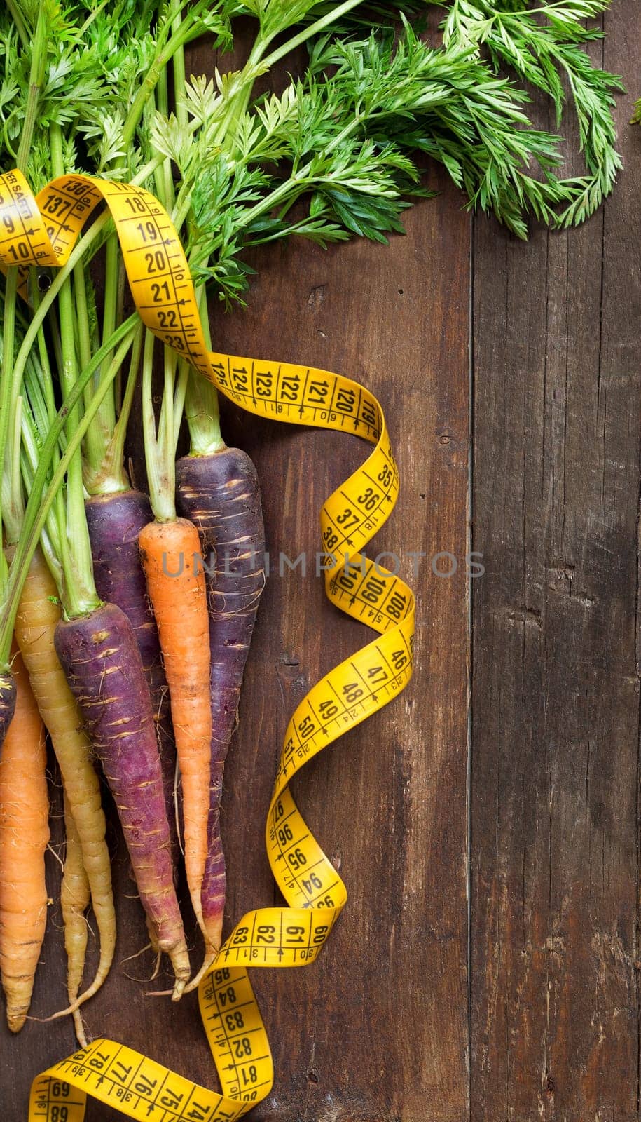 Fresh organic rainbow carrots and yellow measuring type on wood